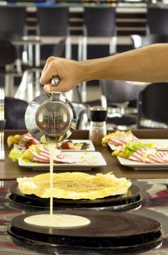 a person is pouring sauce on some food at a table with plates and chairs in the background