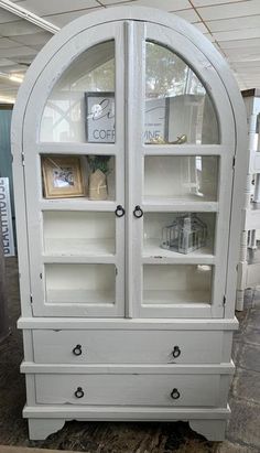 a white china cabinet with glass doors and drawers on the bottom, in a store