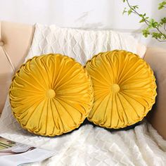 two yellow pillows sitting on top of a couch next to a book and potted plant