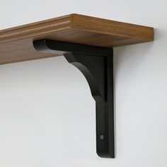 a wooden shelf mounted to the side of a white wall with a black bracket on it