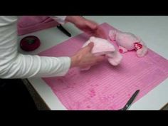 a person cutting paper with scissors and a pink stuffed animal on it's side