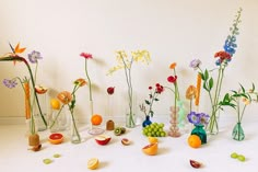 several vases filled with different types of flowers and fruit sitting on a white surface