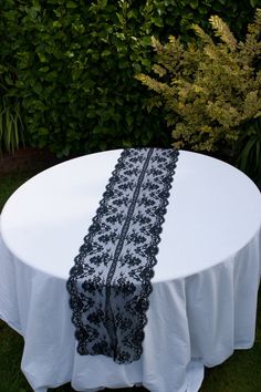 a white table with black lace on it and some bushes in the backgroud