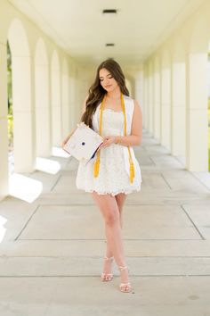 a woman in a white dress and yellow scarf is standing on the sidewalk with her purse