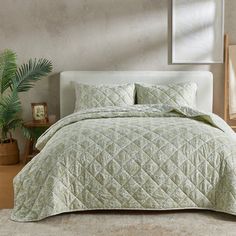 a bed with green bedspread and pillows in a room next to a potted plant