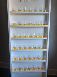 there are many glasses on the shelf with yellow liquid in them and one is empty