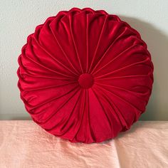 a red round pillow sitting on top of a pink table cloth covered tablecloth with a white wall in the background