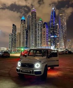 a white truck parked in front of a large city at night with skyscrapers lit up behind it