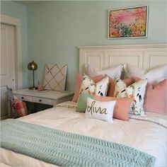 a white bed topped with lots of pillows next to a dresser and desk in a bedroom