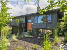 a house that has some plants in front of it and trees around the back yard