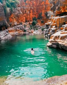 a person swimming in the water near some rocks and cliffs, with a cliff behind them