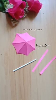 the pink umbrella is next to two sticks and some flowers on a wooden table with measuring tape