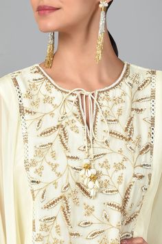 Ivory cape style tunic with zari embroidery, bugle beads and sequin work. Comes with layered sharara.
Component: 2
Pattern: Embroidered
Type Of Work: Zari, Sequin and Beads
Neckline: Round
Sleeve Type: Flared
Fabric: Georgette and Organza
Color: White
Other Details: 
Scalloped hem with shell hangings
Asymmetrical hem
Keyhole front with tie up
Occasion: Sangeet - Aza Fashions Elegant Cape Dress With Zari Work, Elegant Anarkali Set With Cape Sleeves For Festivals, Elegant Festive Sharara With Cape, Elegant Cape-style Sharara For Festive Occasions, Traditional Festive Palazzo Set With Cape, Embellished White Georgette Palazzo Set, White Embellished Georgette Palazzo Set, Traditional Anarkali Set With Intricate Embroidery And Cape Sleeves, Festive Dress With Gota Work And Cape Sleeves