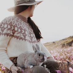 a woman in a hat and sweater holding a rabbit