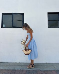 a woman standing in front of a white building holding a basket with flowers on it