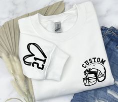 a white shirt with the words custom football on it next to ripped jeans and feathers