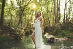 a pregnant woman in a white dress standing on a rock by the water with trees around her