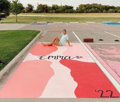 a woman sitting on the ground in front of an empty parking lot with her hand up