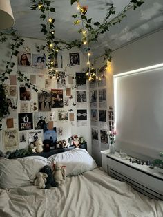 an unmade bed in a bedroom with pictures on the wall and lights strung from the ceiling