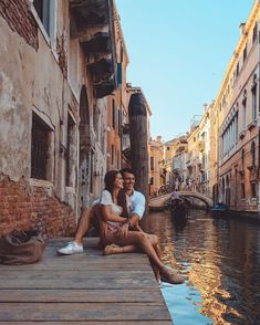 a man and woman sitting on a dock next to buildings in venice, italy by the water