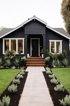 a black house with white trim and plants on the front lawn, along with steps leading up to it