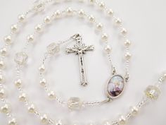 "- Personalized handmade rosary made with white Czech glass pearls and big white Czech cathedral glass beads - Choice of medals and letters - Comes with a velour pouch and gift box This white handmade baptism rosary is made with white Czech glass pearls and crystals and big antique looking Czech cathedral beads. It has a beautiful vintage look. Comes with your choice of Baptism, First Communion, Confirmation, or other medals. Read below for details. Over 80 colorful designs to choose from. Enter Pearl Rosary For First Communion, Spiritual Style, White Rosary Bracelet For First Communion, Spiritual Pearl Rosary For First Communion, Pearl White Rosary For First Communion, White Pearl Rosary Bracelet For Baptism, White Cross Rosary Bracelet For First Communion, Silver Beaded Rosary For First Communion, White Rosary With Round Beads For Confirmation, White Cross Rosary Bracelet For Confirmation