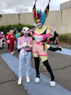 two people in costume standing next to each other on the sidewalk with clowns behind them