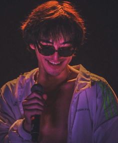 a shirtless man wearing sunglasses holding a microphone