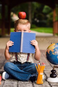 a little boy sitting on the ground with an apple on top of his head reading a book