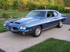 a blue muscle car parked on the side of a driveway in front of a house