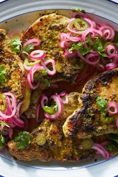 a white plate topped with meat covered in onions and green garnish next to sliced radishes