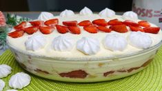 a cake with strawberries and whipped cream on top sitting on a green place mat