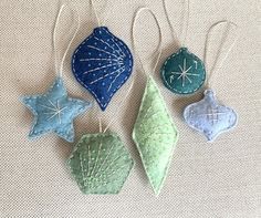 three ornaments are hanging from strings on a white cloth surface, one is blue and the other is green