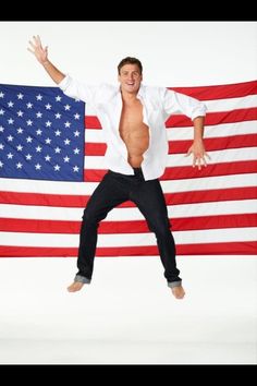 a shirtless man is jumping in front of an american flag with his arms outstretched