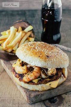 a sandwich and fries on a wooden cutting board with a bottle of soda in the background