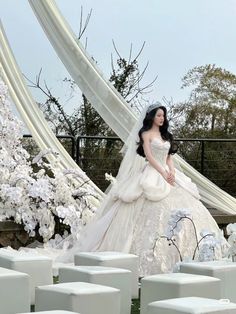 a woman in a white wedding dress standing next to some chairs and flowers on the ground