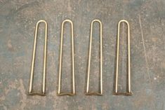 four brass metal hooks sitting on top of a cement floor