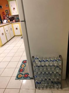 a refrigerator with several empty water bottles on the floor next to it and a rug in front of it