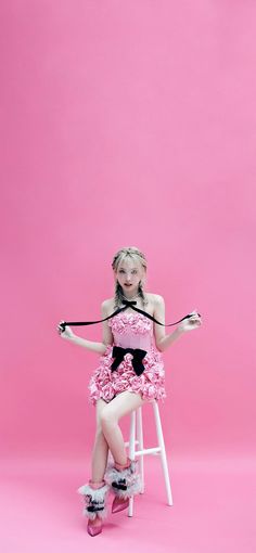 a woman sitting on top of a white stool wearing a pink dress and black bow tie