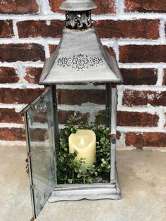 a lit candle is sitting in front of a brick wall with greenery on it