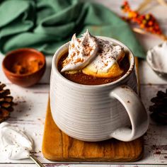 a mug filled with hot chocolate on top of a wooden cutting board next to pine cones