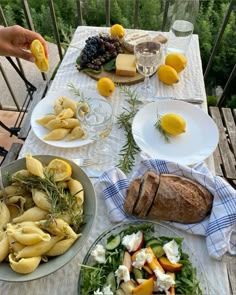 a table topped with plates of food next to a bowl of fruit and bread on top of a wooden table