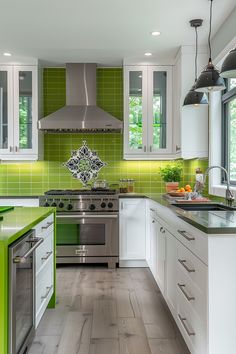 a green and white kitchen with stainless steel appliances, wood flooring, and tile backsplash