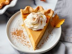 a slice of pumpkin pie on a white plate with whipped cream and leaves around it