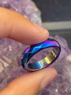 a person holding a ring in their hand on top of some rocks and purple crystals