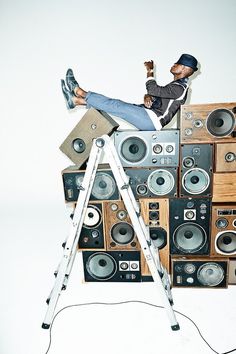 a man sitting on top of a ladder next to a pile of stereo speakers and amps