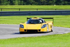 a yellow sports car driving on a race track with grass and trees in the background