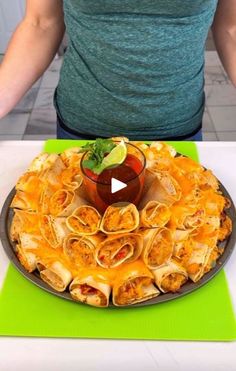 a person standing in front of a platter of food on a table with a green mat