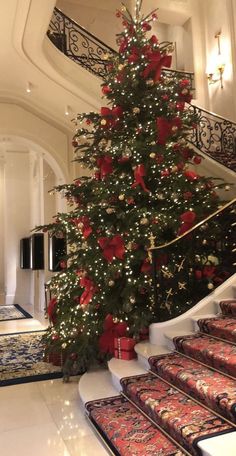 a decorated christmas tree sitting in the middle of a living room next to a stair case