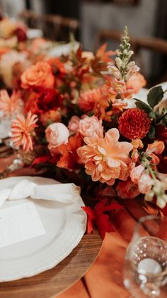 the table is set with white plates and orange napkins, red flowers, and greenery